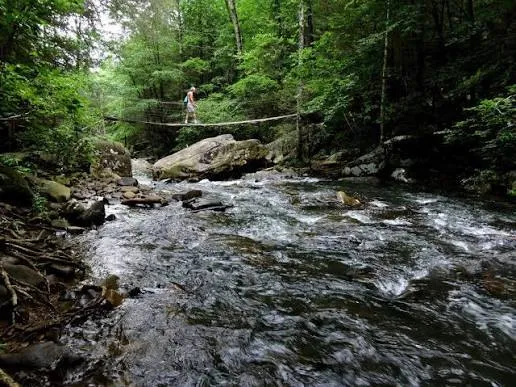 Hiker crossing the suspension bridge over the creek at Rainbow Lake Wilderness Park
