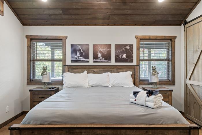 A bedroom with a large bed, wooden headboard, two bedside tables with lamps, and three wall-mounted artworks.