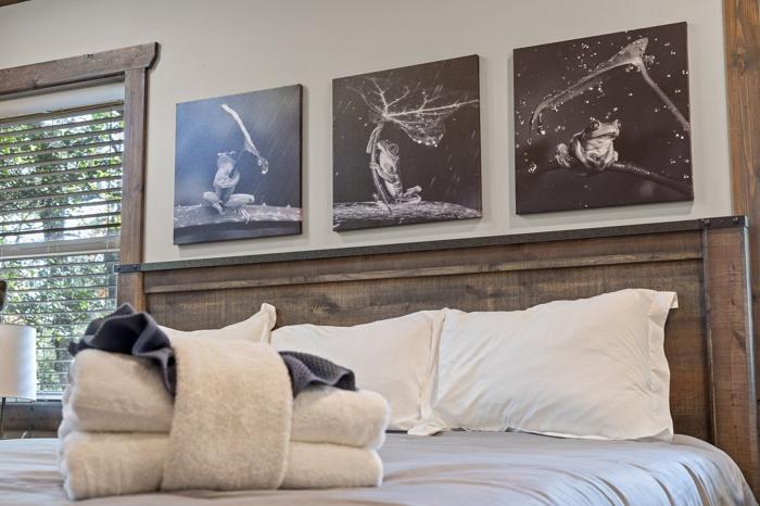 A bed with white linens, a wooden headboard, and three artworks on the wall.
