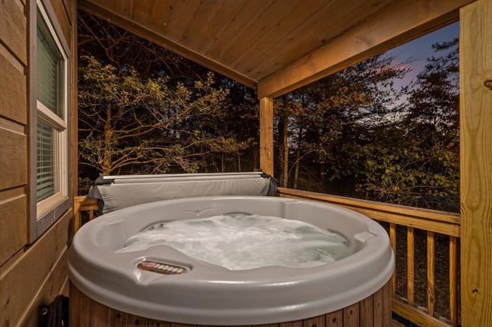 A hot tub on a wooden deck with a view of trees and a sunset.
