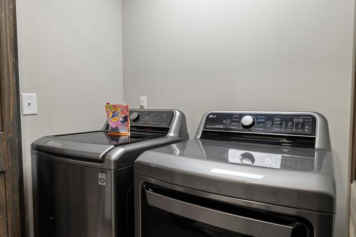 A laundry area with two stacked washers and dryers, a power outlet, and a box of Tide detergent.