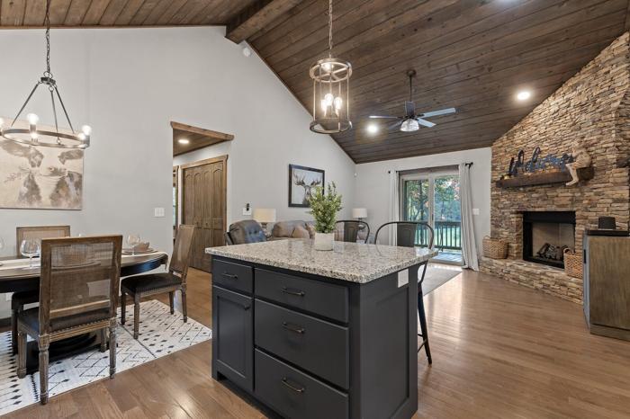 A spacious kitchen with a large island, wooden ceiling, and a stone fireplace.