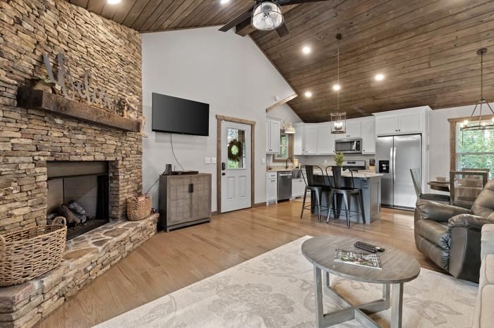 A spacious living area with a stone fireplace, a flat-screen TV, a kitchen with modern appliances, and a dining area with bar stools.