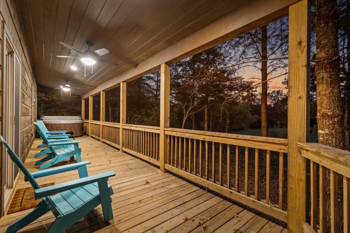 A wooden deck with benches, a ceiling fan, and a view of trees.