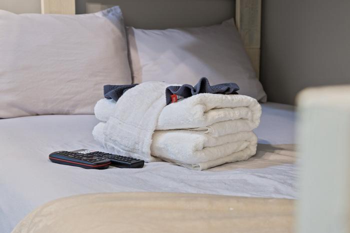 A neatly made bed with a folded towel, a remote control, and a pillow.