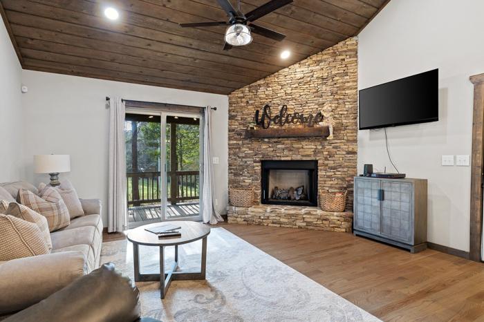 A living room with a stone fireplace, a ceiling fan, a flat-screen TV, a sofa, and a coffee table.