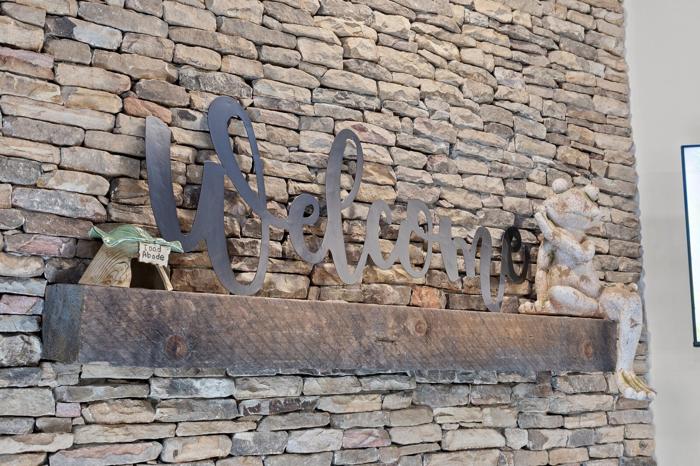 A stone wall with a metal welcome sign and a wooden shelf with a sign reading &lsquo;Food Abode.&rsquo;