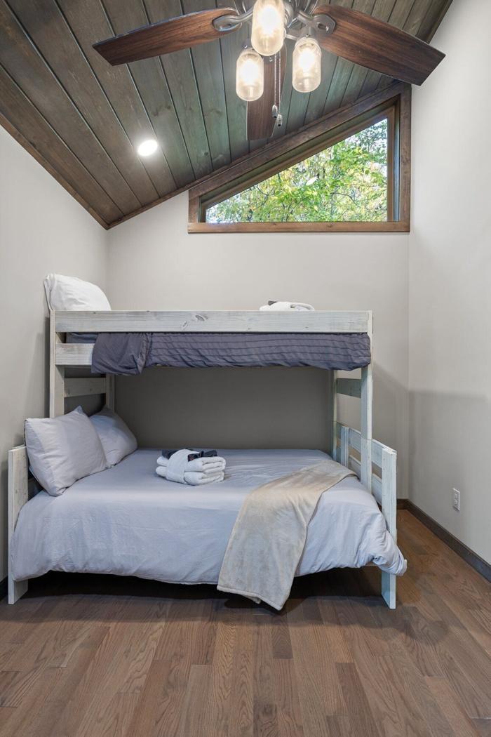 A bunk bed with a window, wooden ceiling, and a ceiling fan.