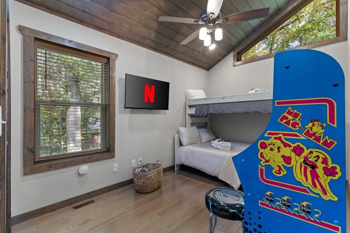 A room with a bunk bed, a TV mounted on the wall, a ceiling fan, and a window with blinds.