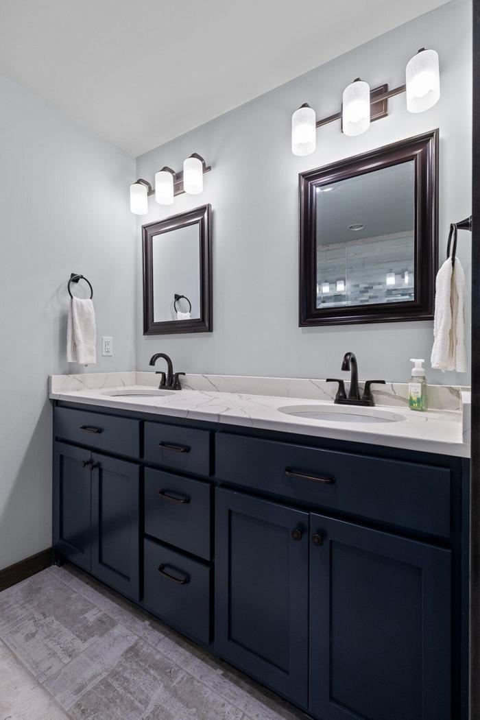 A bathroom with two sinks, dark cabinets, and a large mirror with light fixtures above.