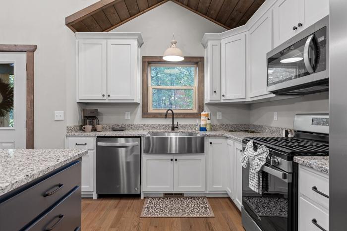 A kitchen with white cabinets, a stainless steel dishwasher, a black stove, and a window with a view of trees.