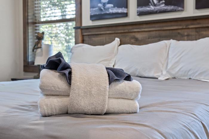 A neatly made bed with folded towels and a blanket, a wooden headboard, and framed artwork on the wall.